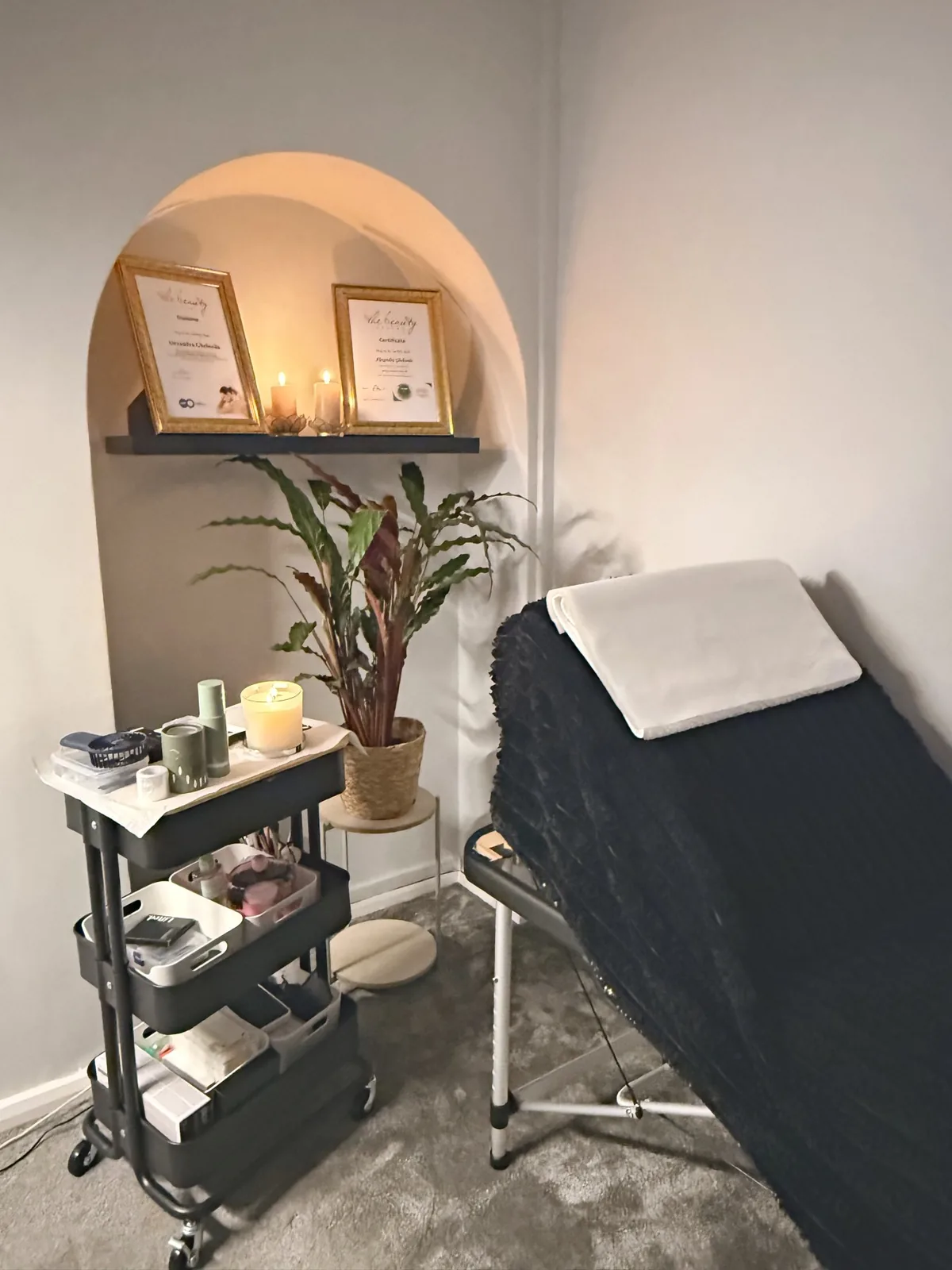 Candlelit treatment room with lash bed, plant and certificates